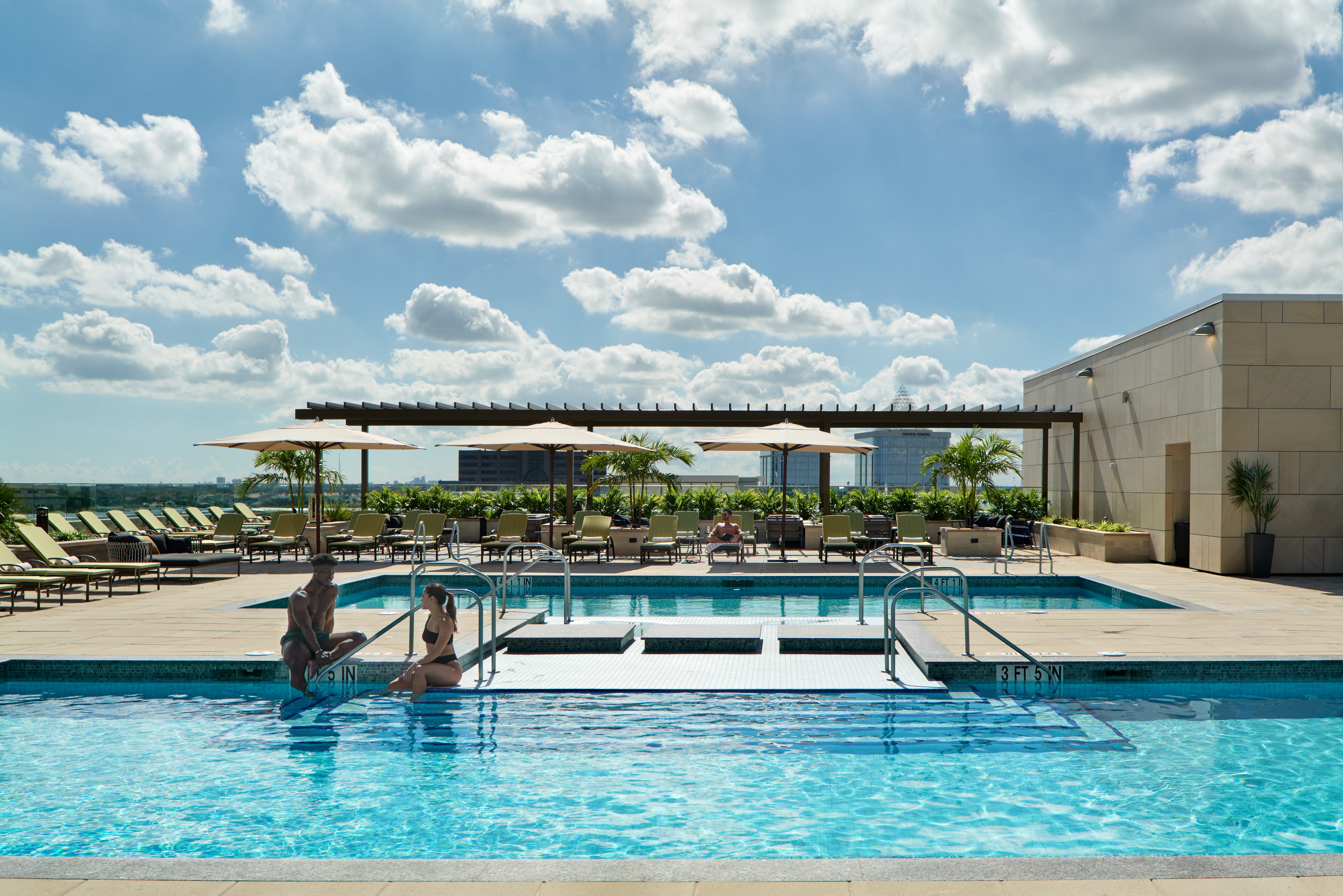 2 people enjoy a sparkeling outdoor pool and deck area with lounge chairs