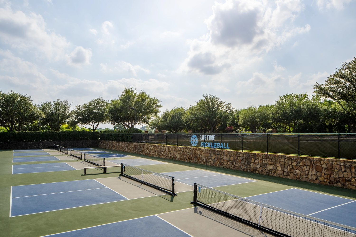 Pickleball courts at the club, surrounded by greenery, located at the edge of a serene landscape.