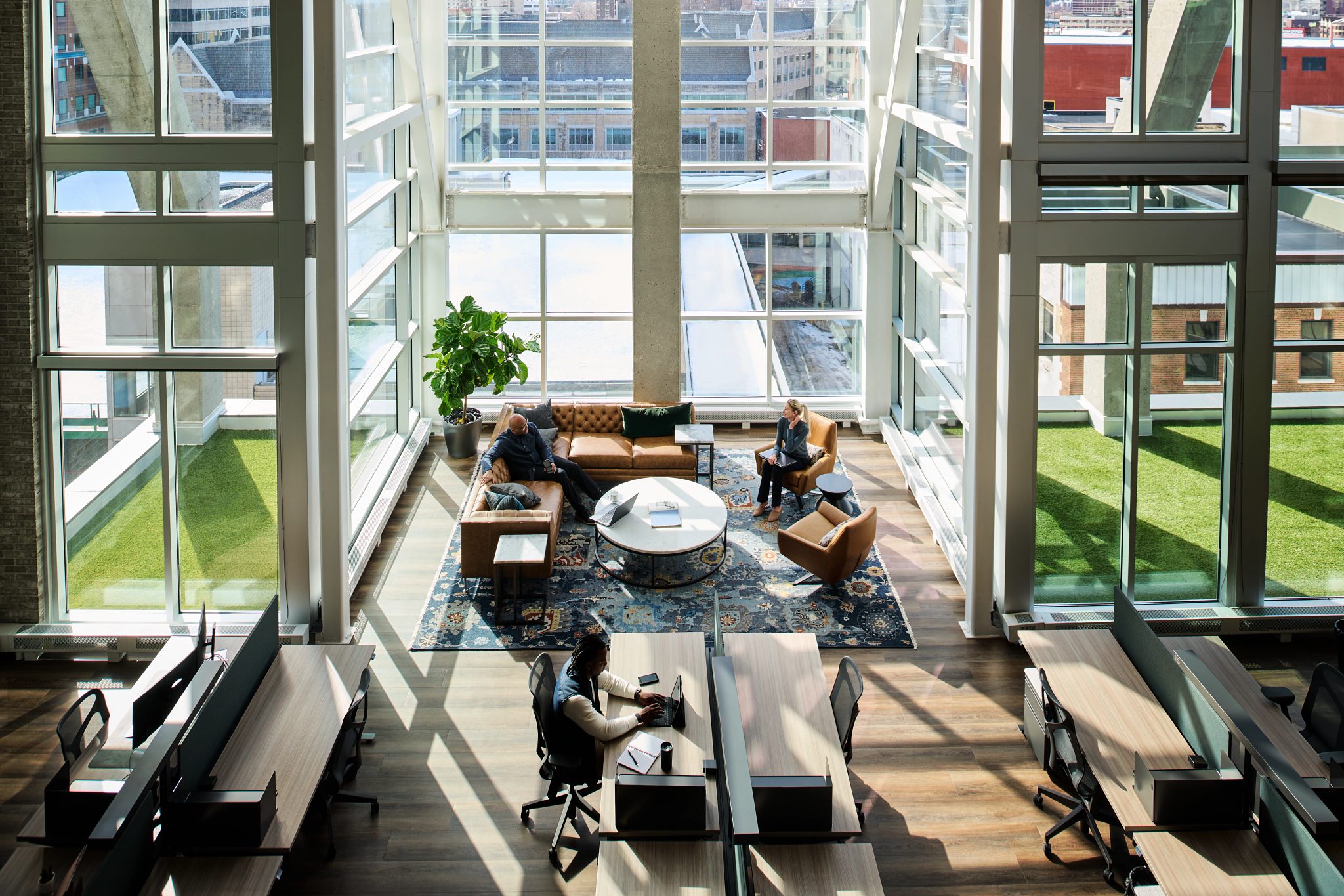 Windows spanning floor to ceiling let in light in a coworking area with couches and desks