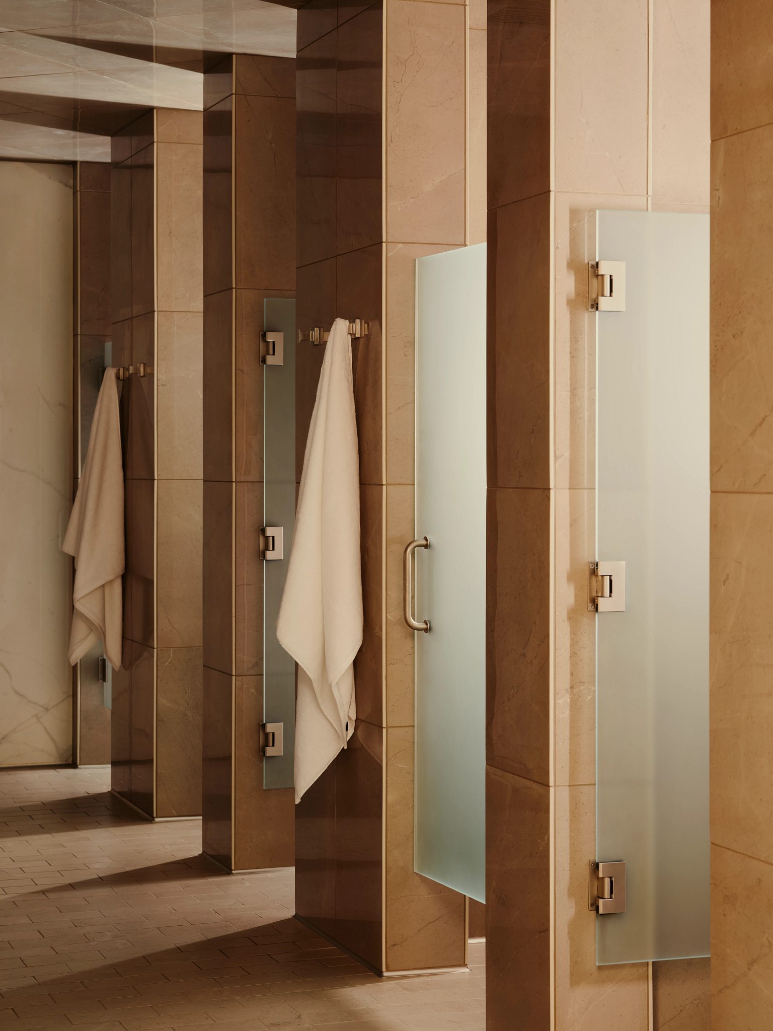 Row of showers with towels hanging on hooks in the locker room at Life Time Atlantic Avenue club location