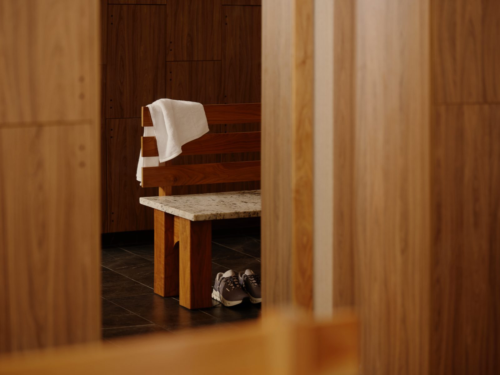 A towel and tennis shoes on a bench next to a bay of lockers in the Life Time Atlantic Avenue club location.