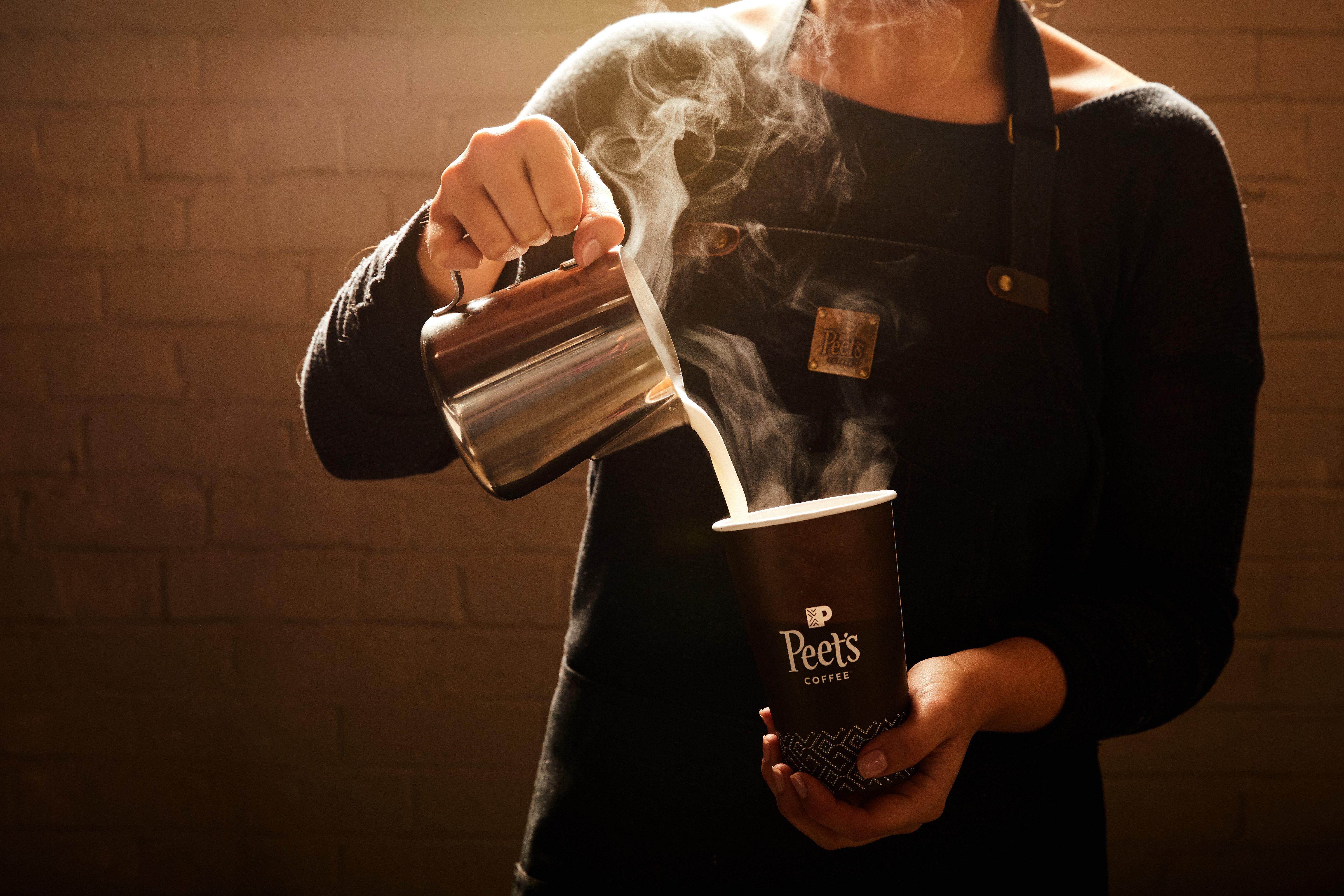 A barista pours steamed milk into a Peet's coffee cup