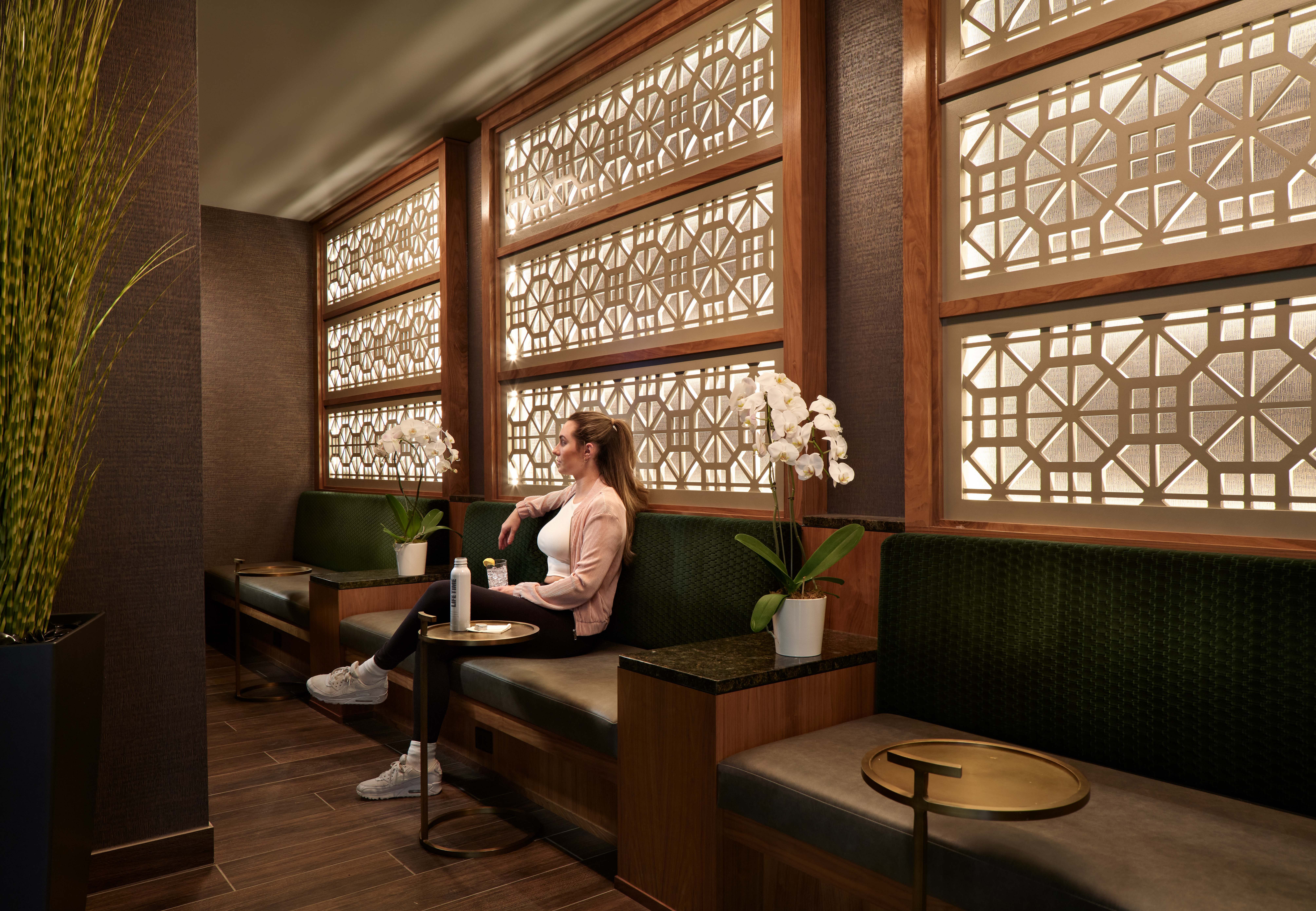 A Life Time member sitting on a bench drinking a glass of water in the lounge