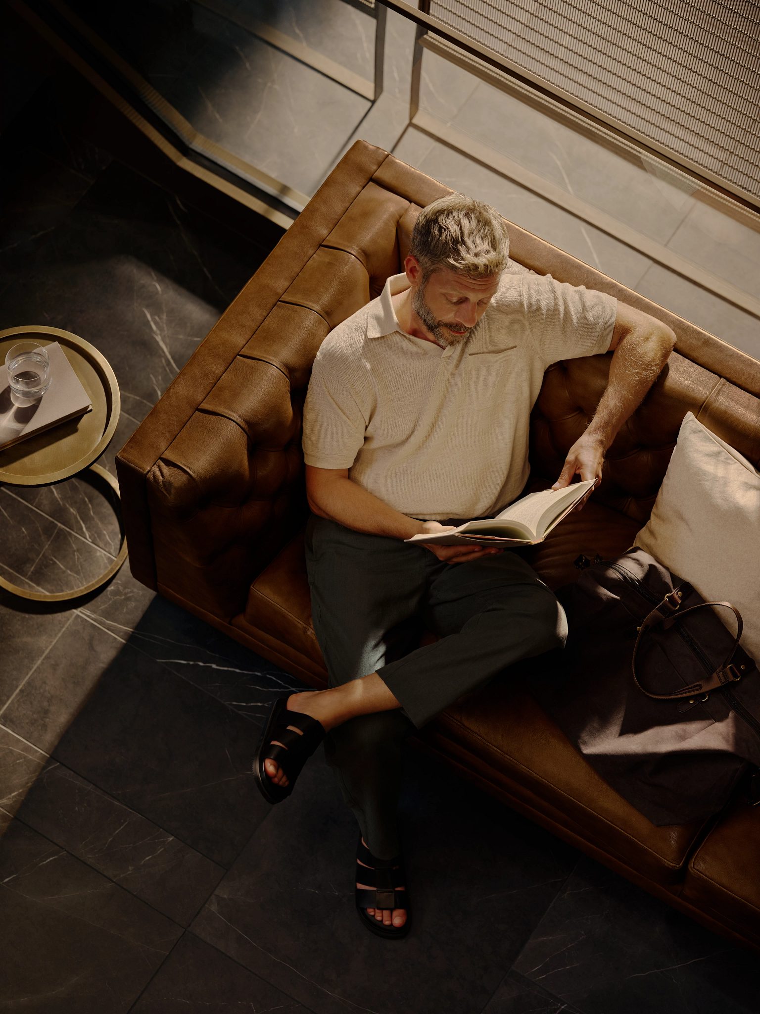 Overhead view of a man sitting on a leather couch relaxing reading a book