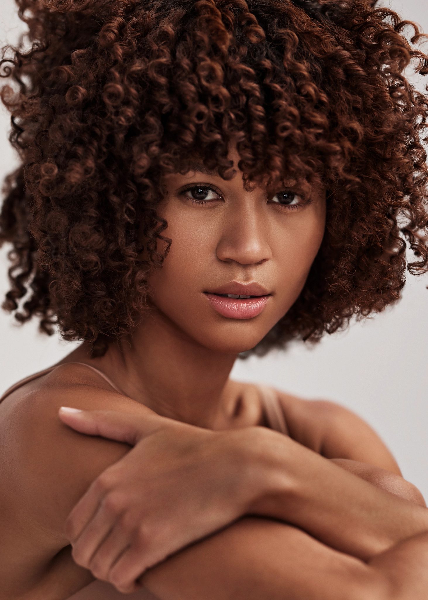 Close-up portrait of an attractive female with curly brunette hair looking directly at the camera, showcasing her flawless skin