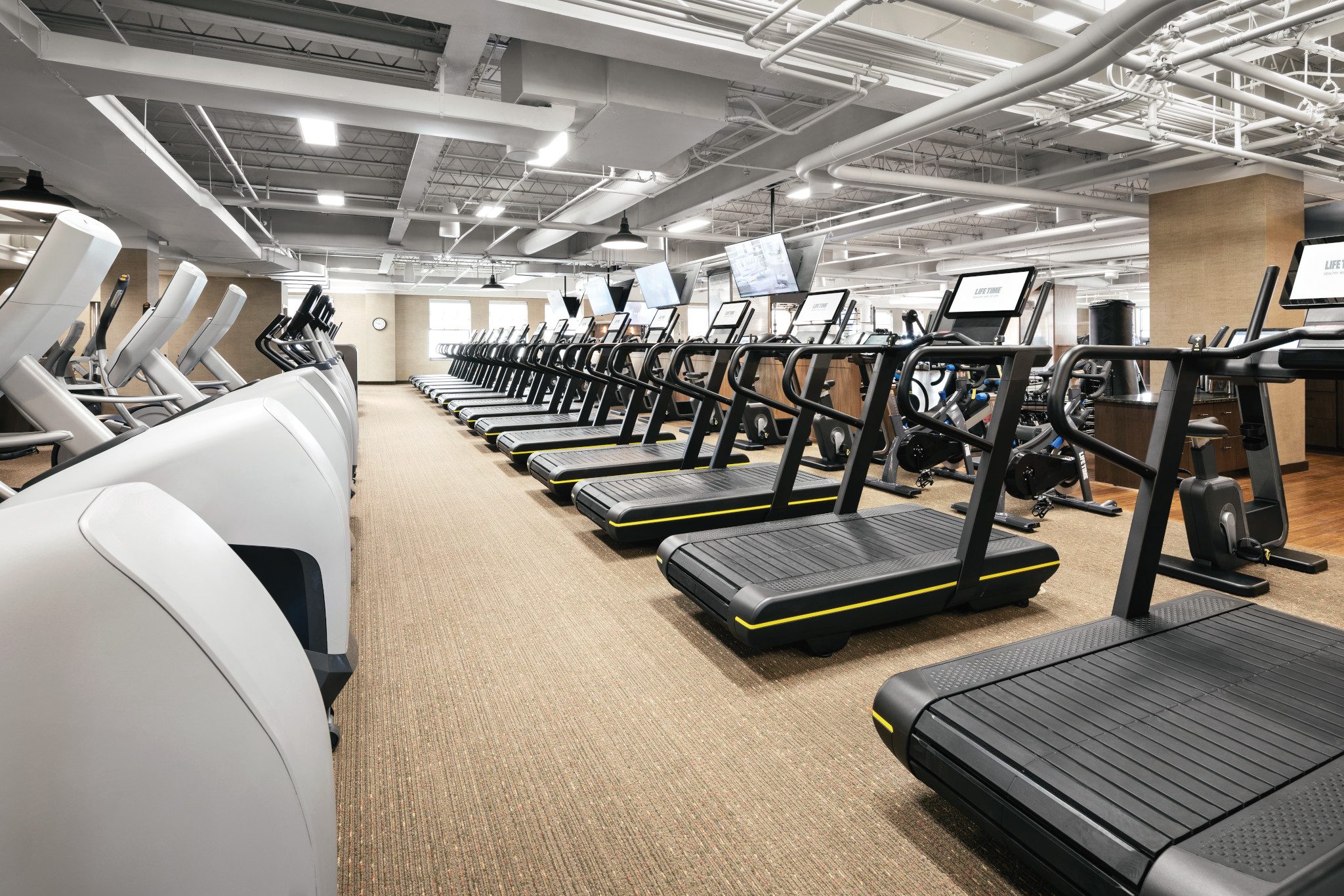 A carpeted fitness floor with rows of treadmills and other cardio equipment