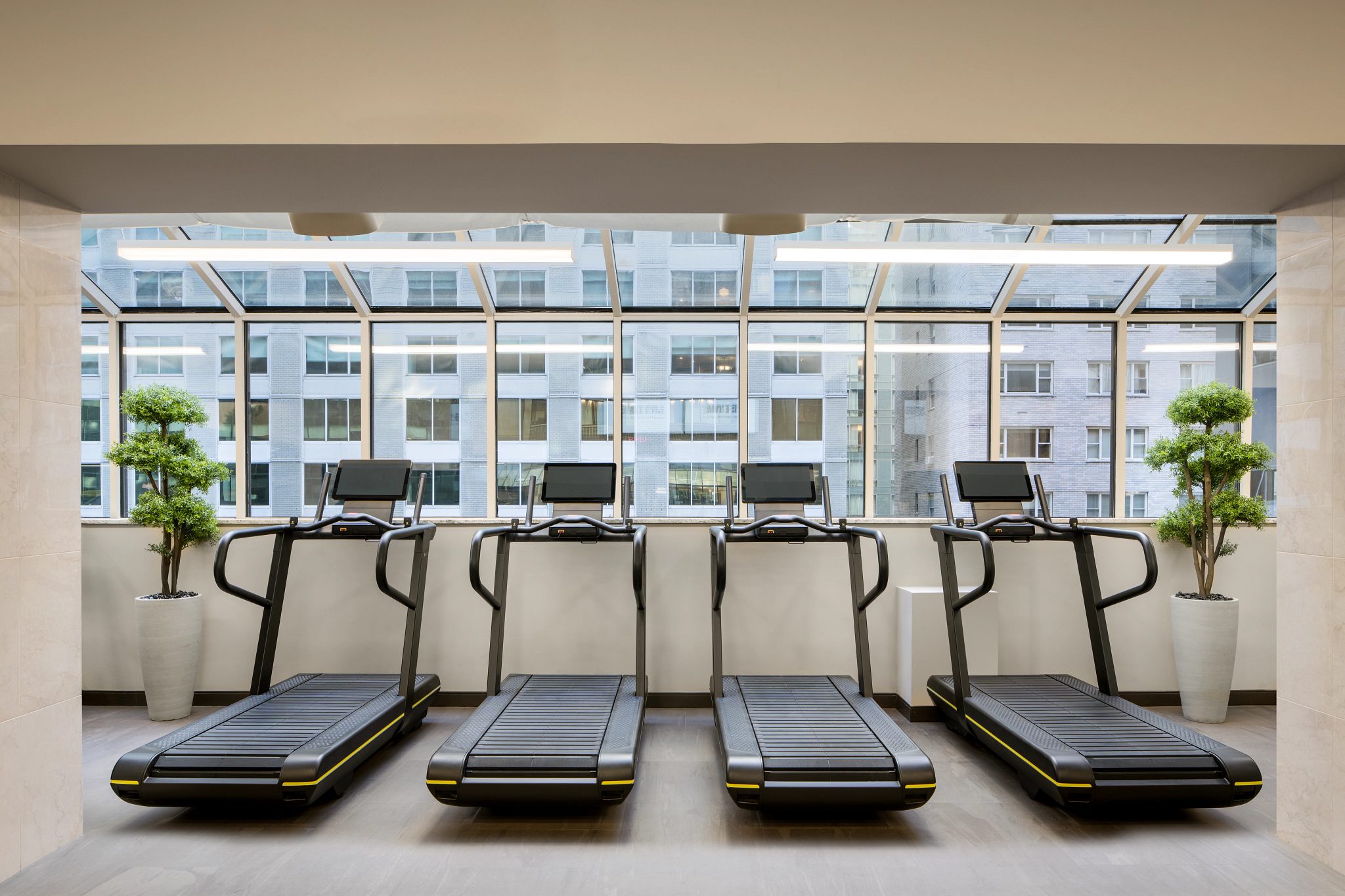 Row of treadmills facing windows leading out to an urban setting