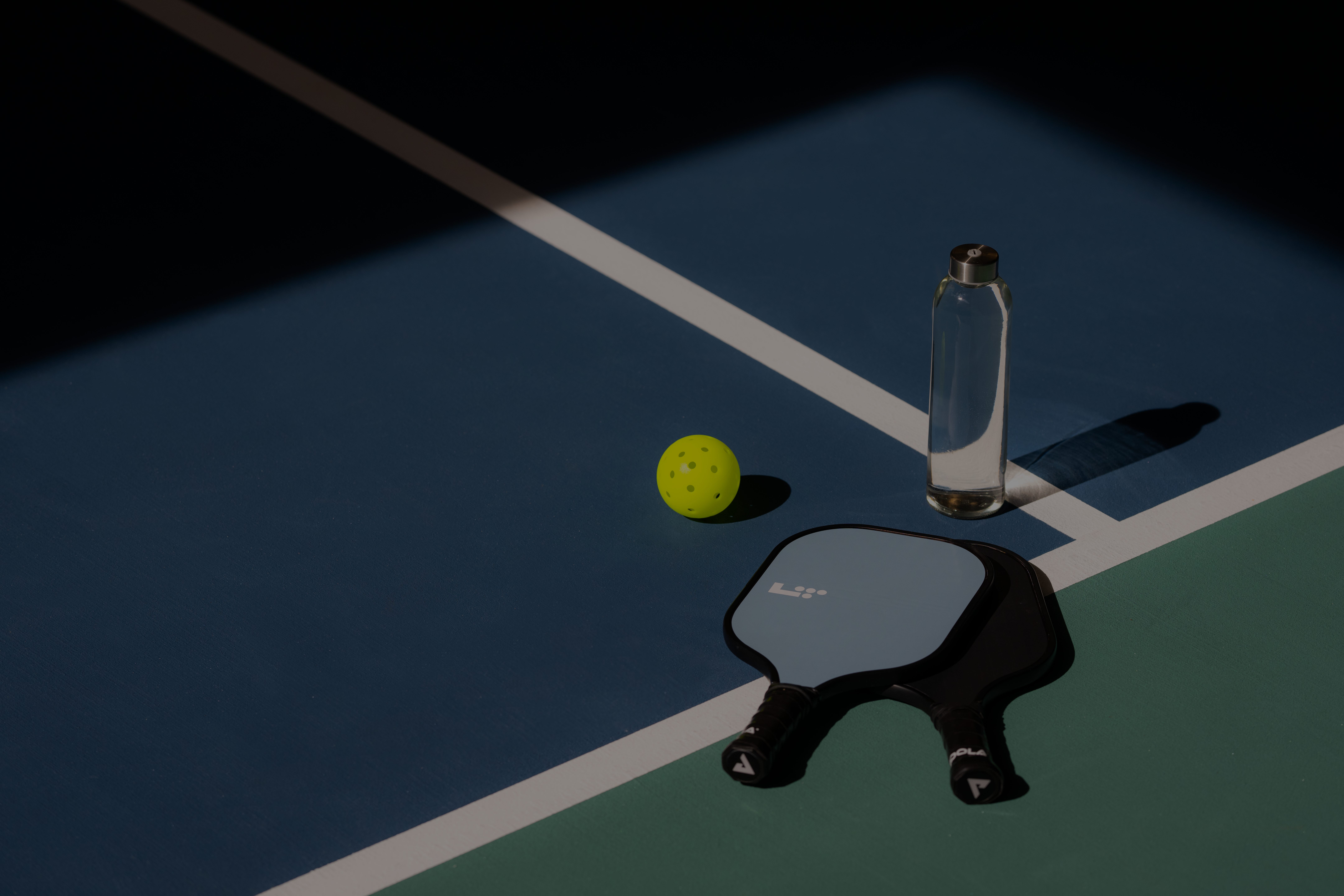 a pickleball, paddle and water bottle sitting on a pickleball court