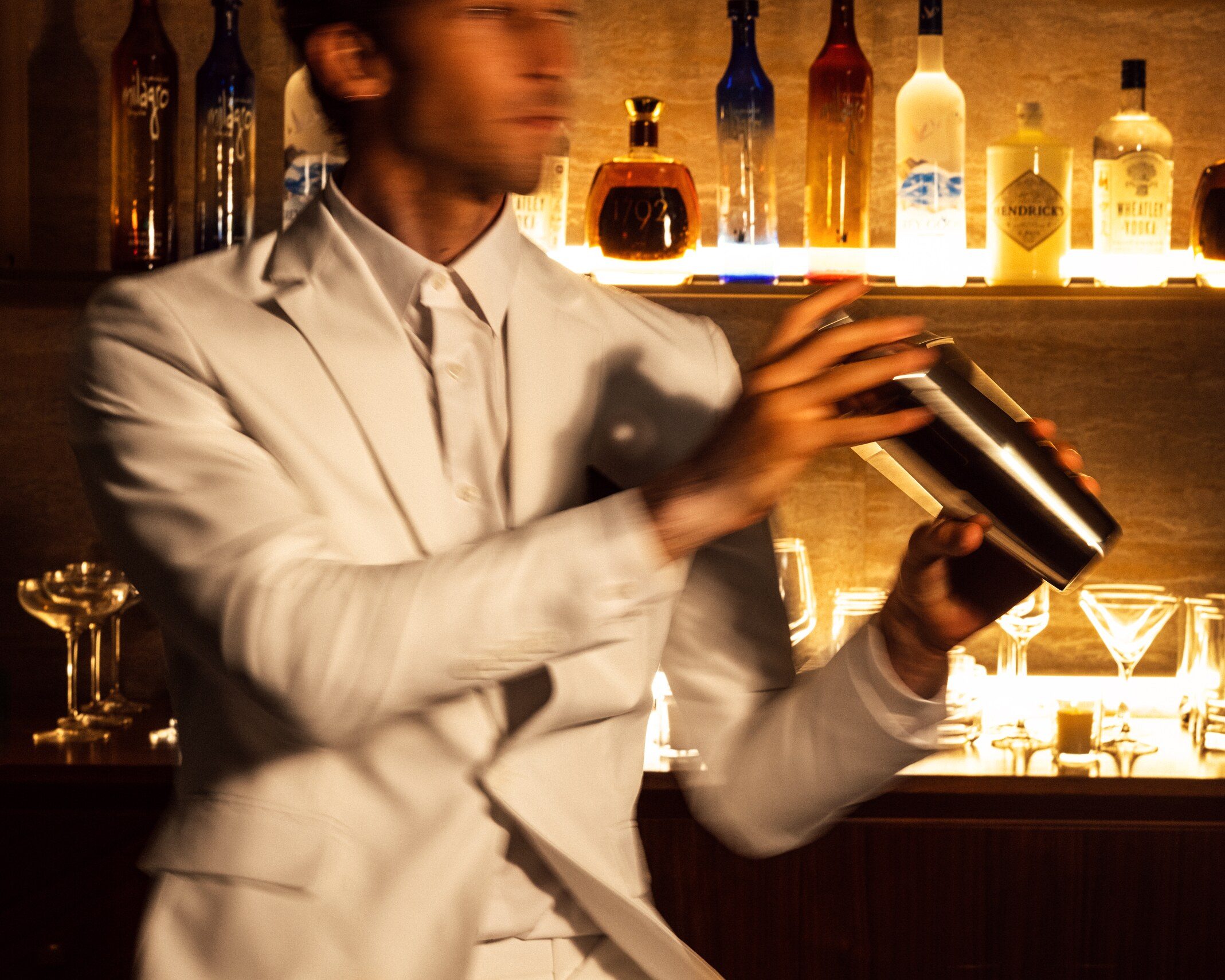 Expert bartender crafting cocktails behind bar - mixologist in professional attire preparing drinks with premium spirits collection.