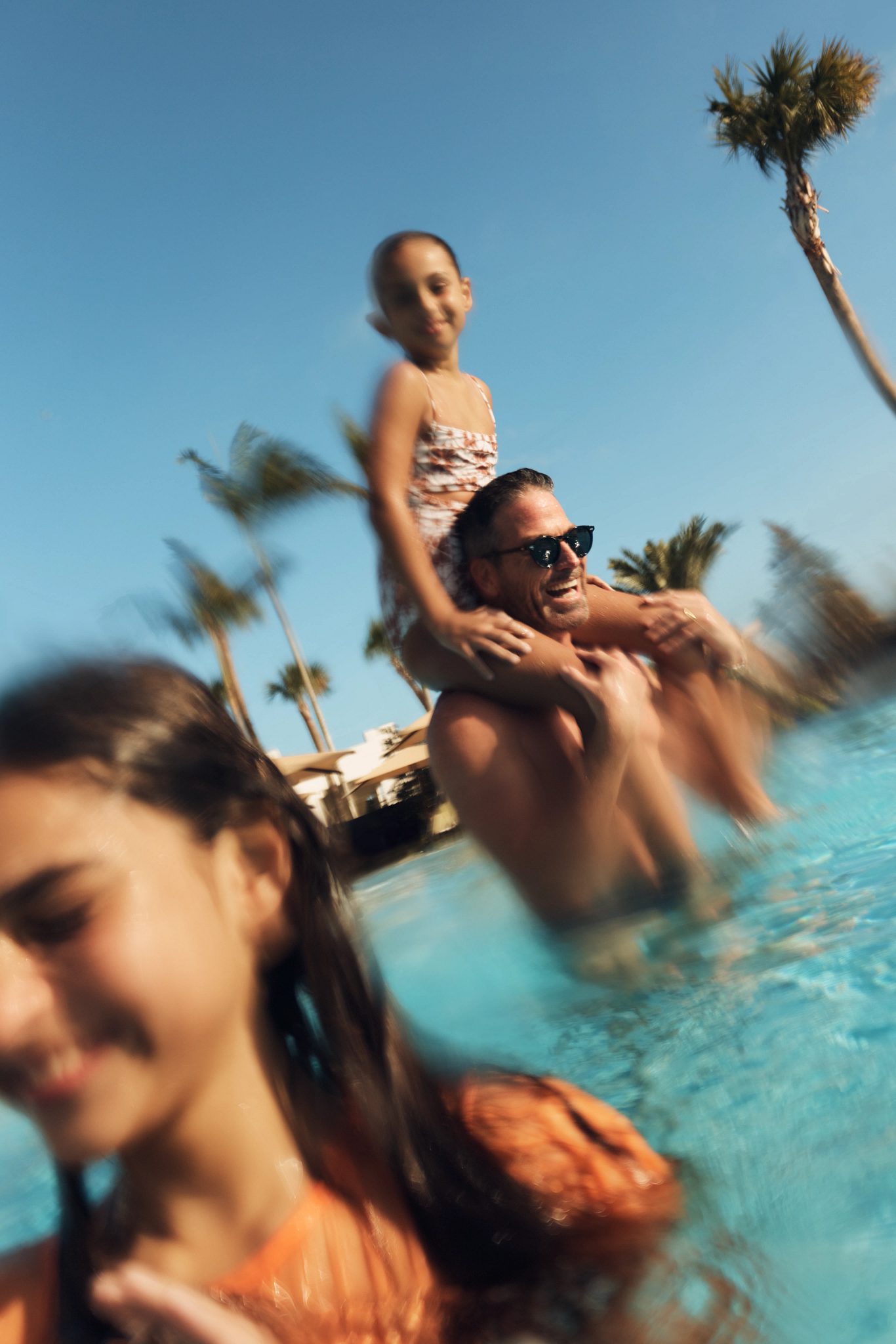 man in a pool with his daughter on his shoulders