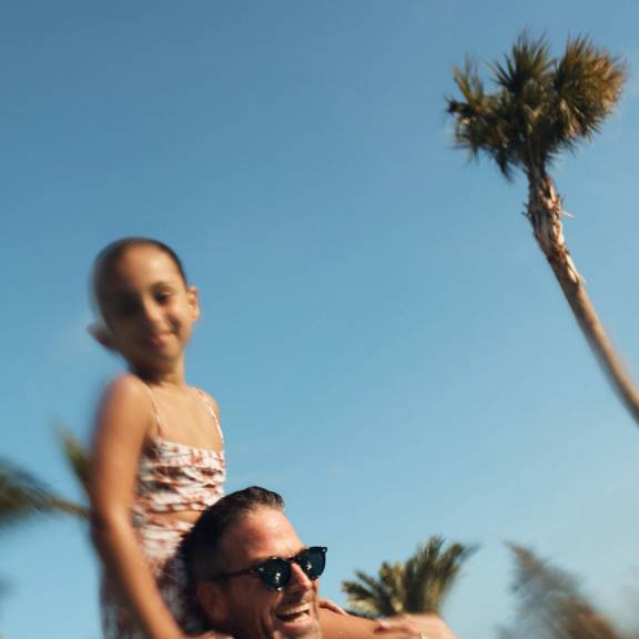 man in a pool with his daughter on his shoulders
