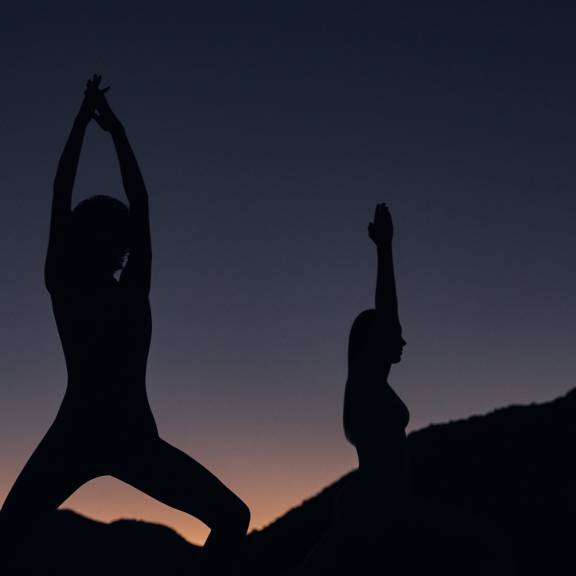 Two silhouetted females doing yoga poses on a beach