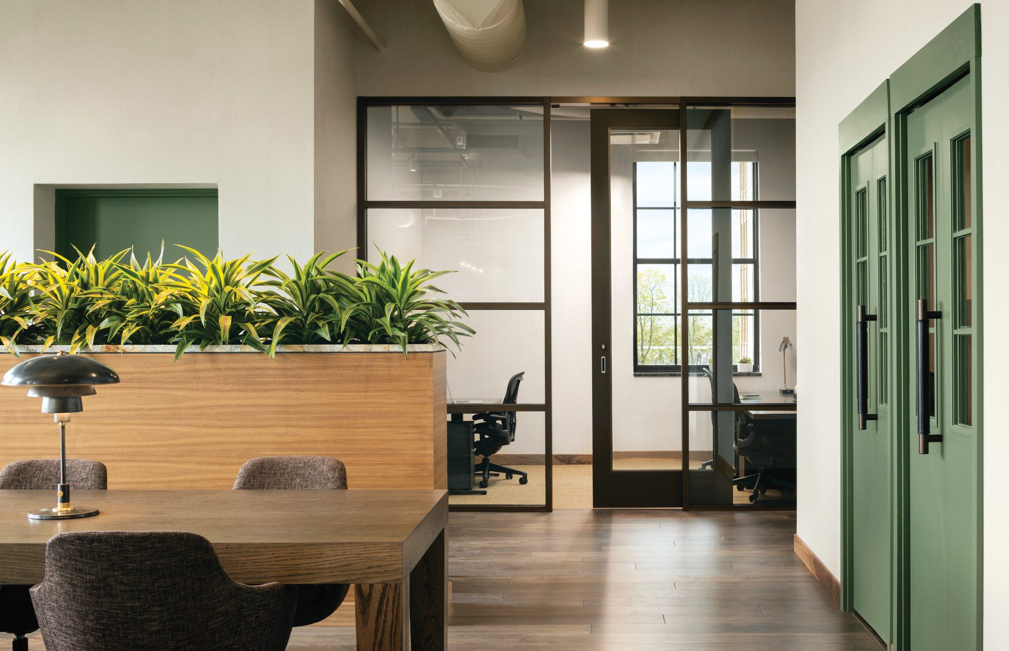 A wooden table with desk chairs next to an open conference room with glass doors and windows