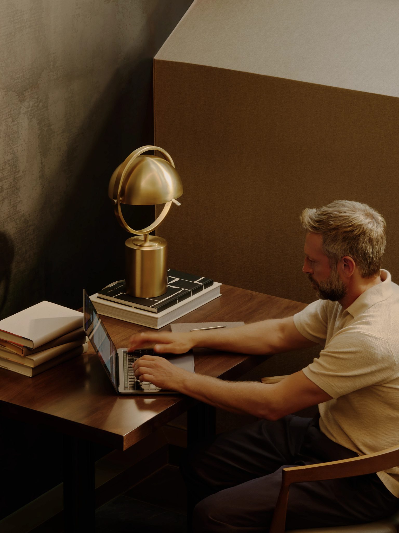 A man sitting at a desk working on his laptop surrounded by stacks of books