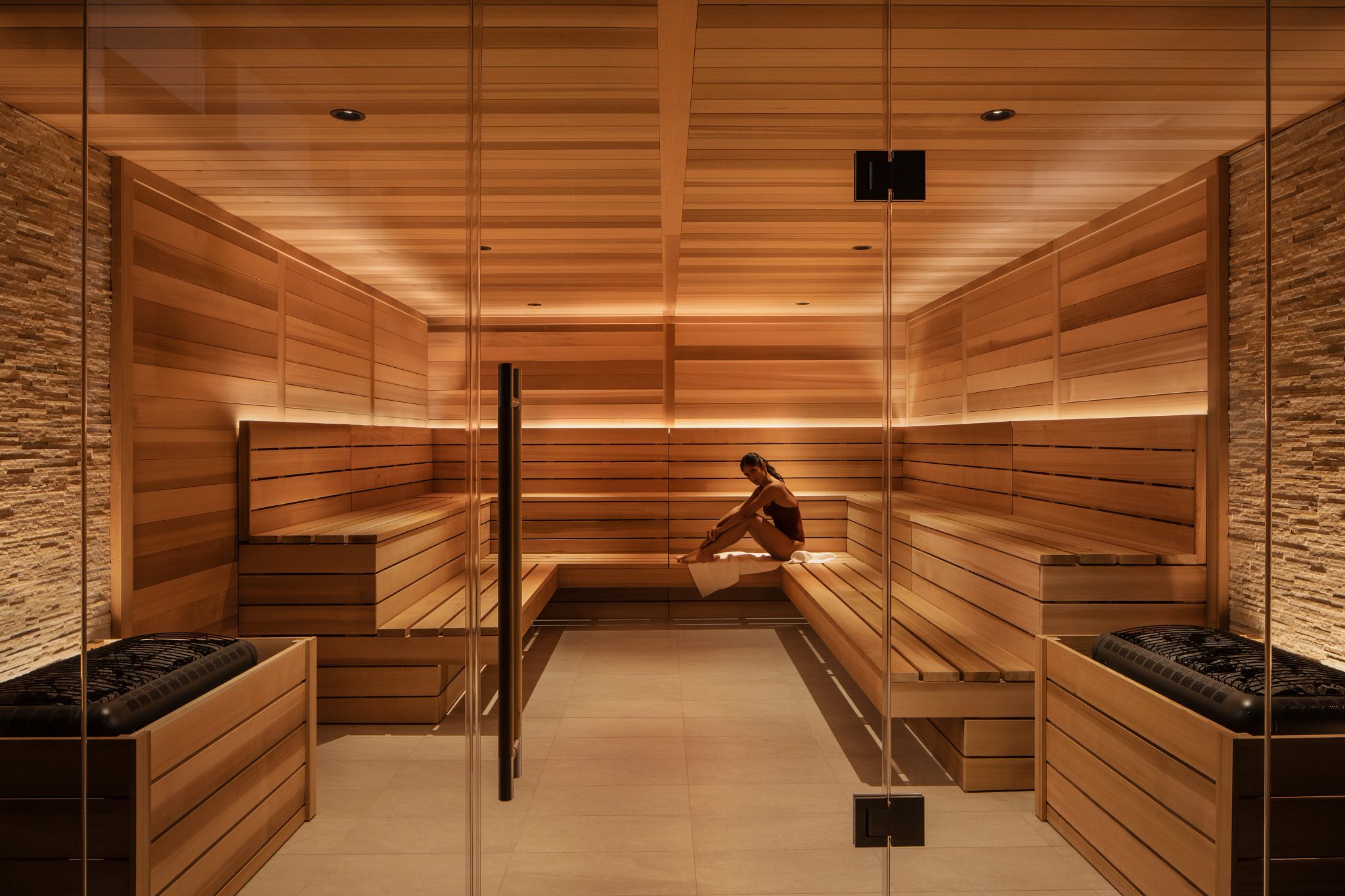 A woman wearing a bathing suit sitting in a dry sauna looking directly at the camera