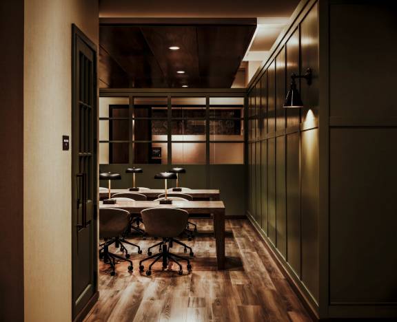 Life Time Work lounge work space, two long tables with lamps on a wood floor and a nice green shleves and walls.