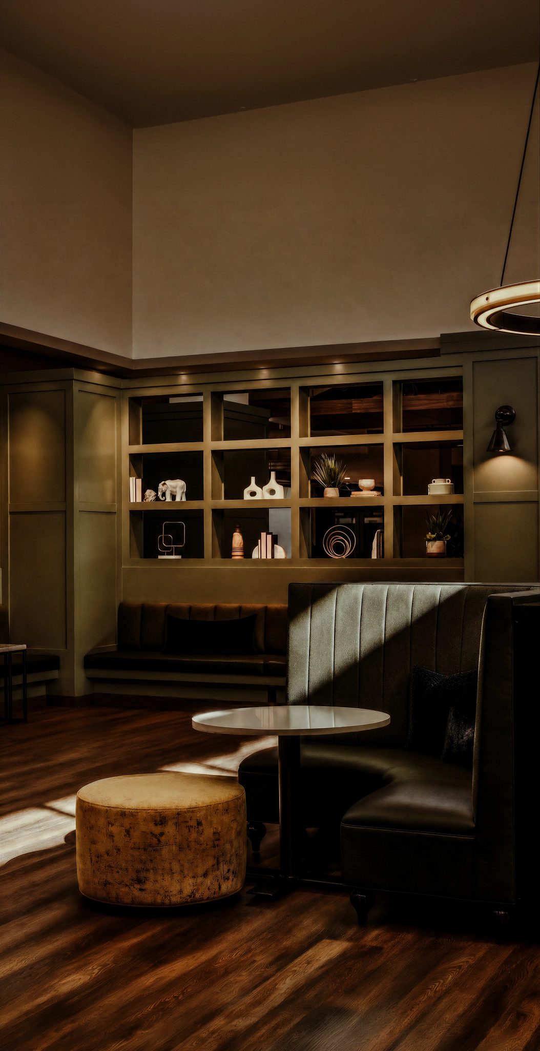A seating area at Life Time Work with a booth along the back wall with knick-knacks on the sheves. A curved booth with a table and round fabric stool beside the table.