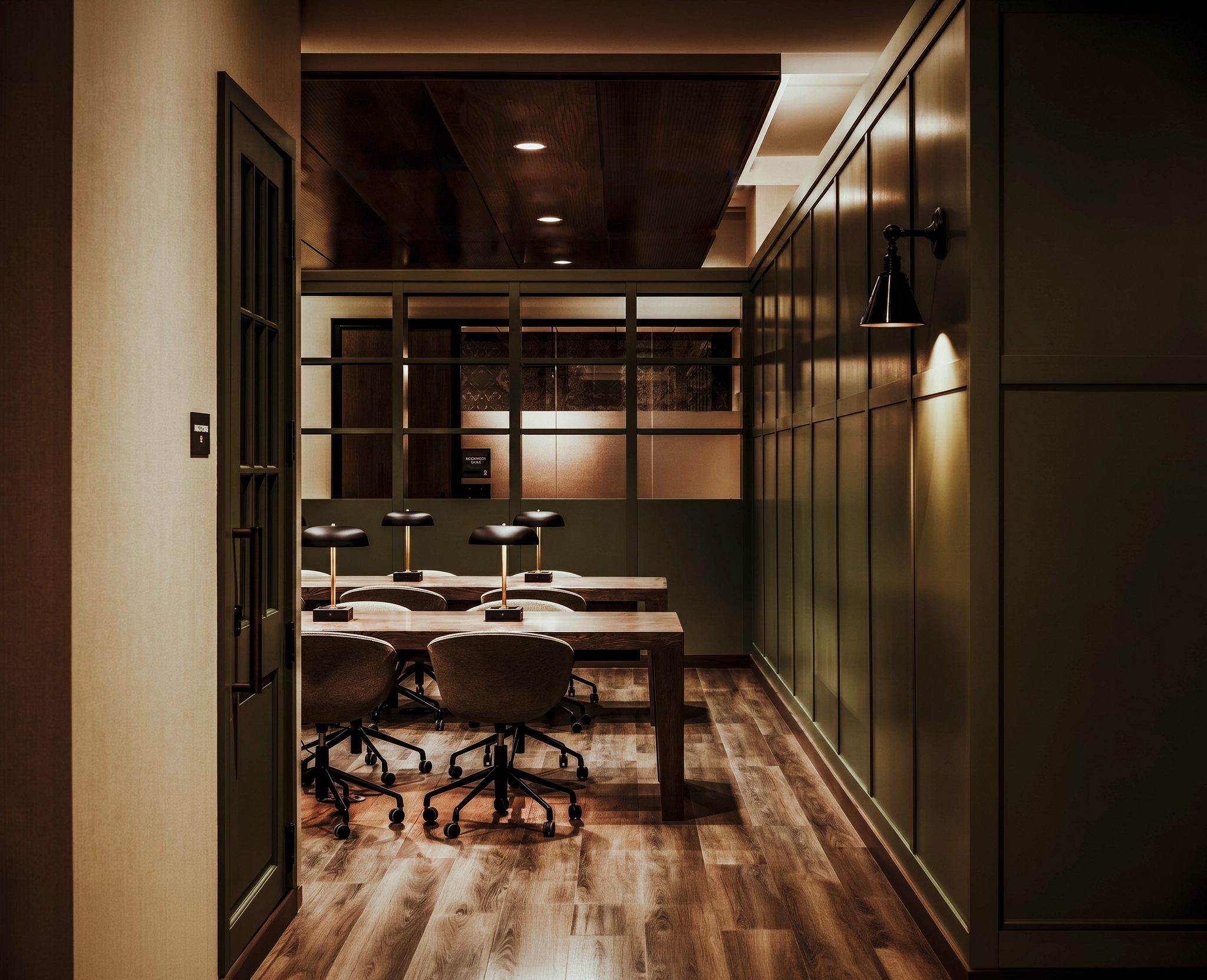 Life Time Work lounge work space, two long tables with lamps on a wood floor and a nice green shleves and walls.