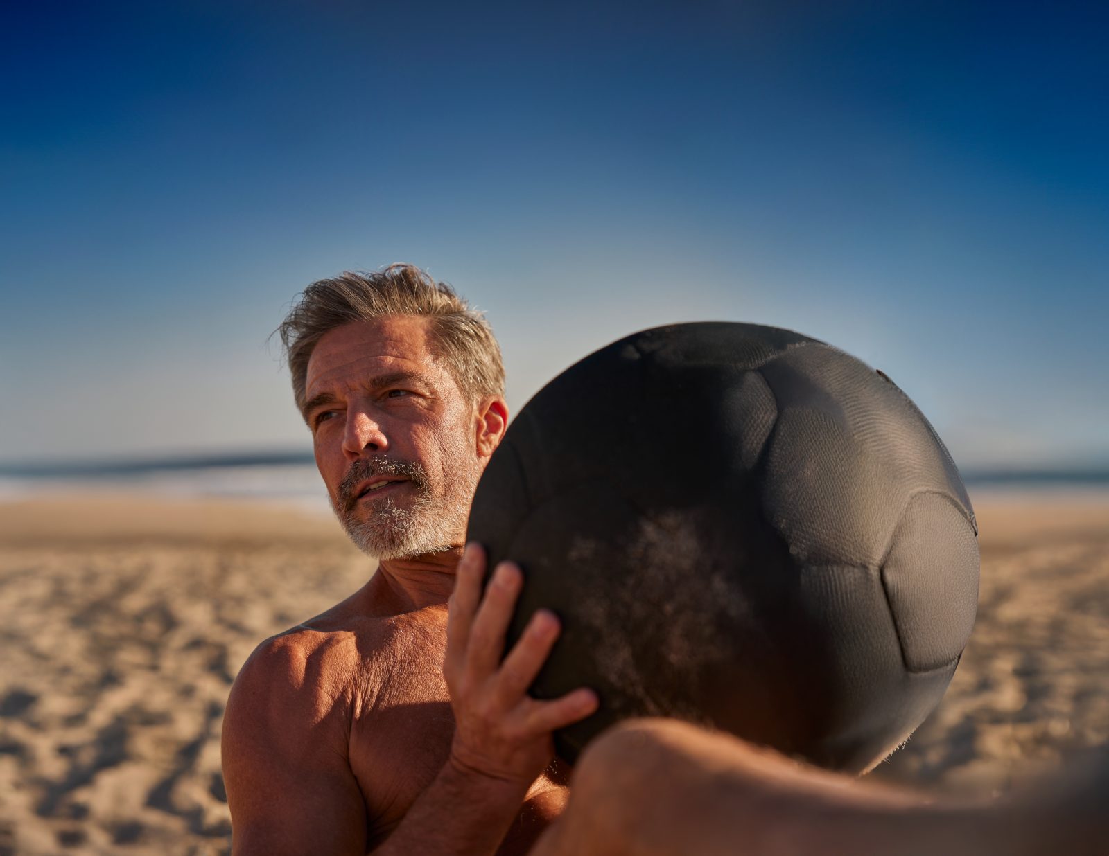 Mature man exercising with a weighted ball on the beach