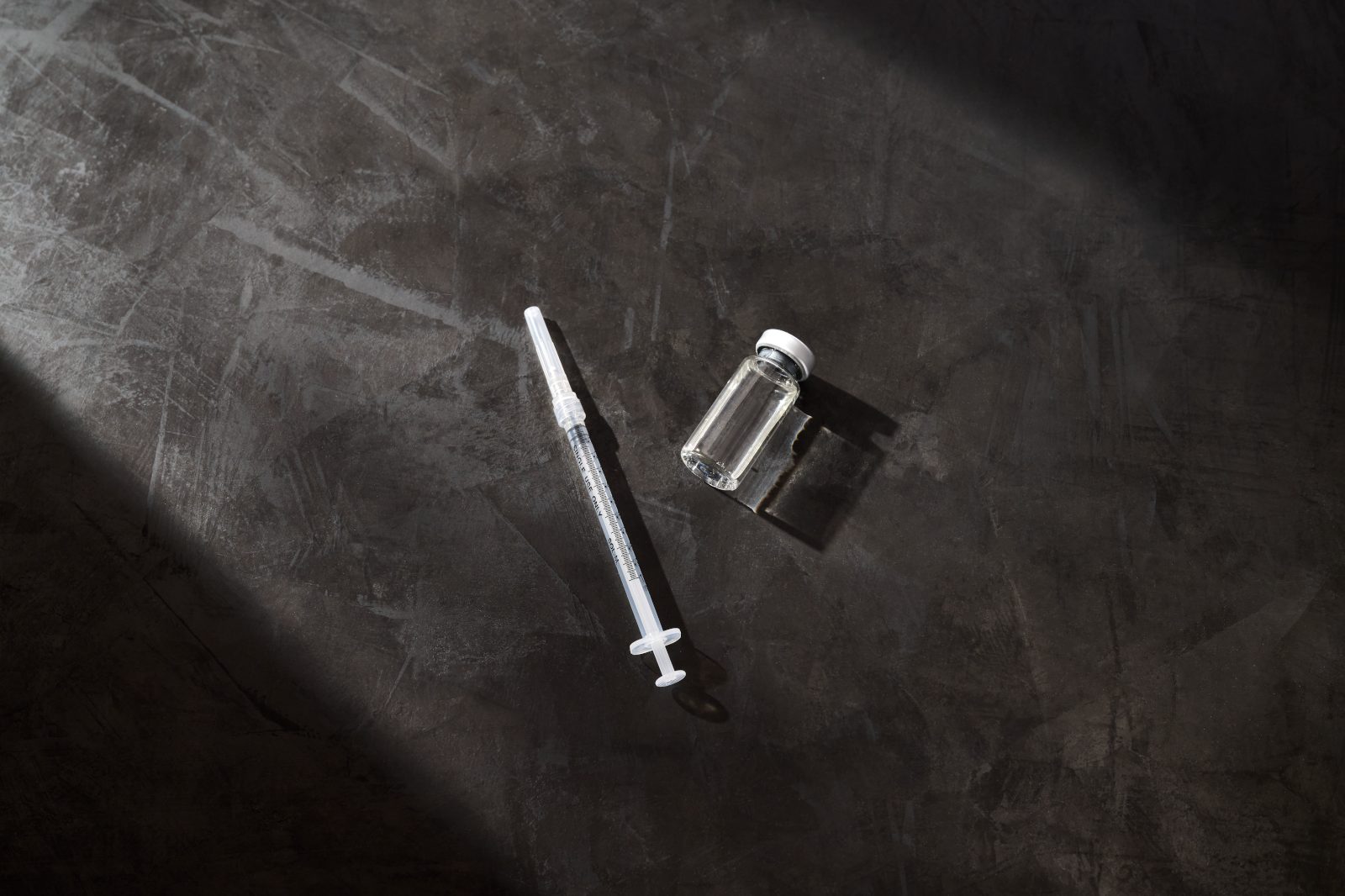 A syringe and clear glass vial on top of a dark gray background